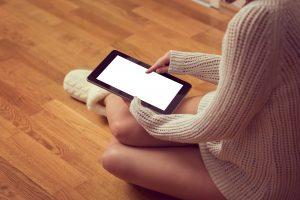 une femme assise au sol utilisant une tablette numérique