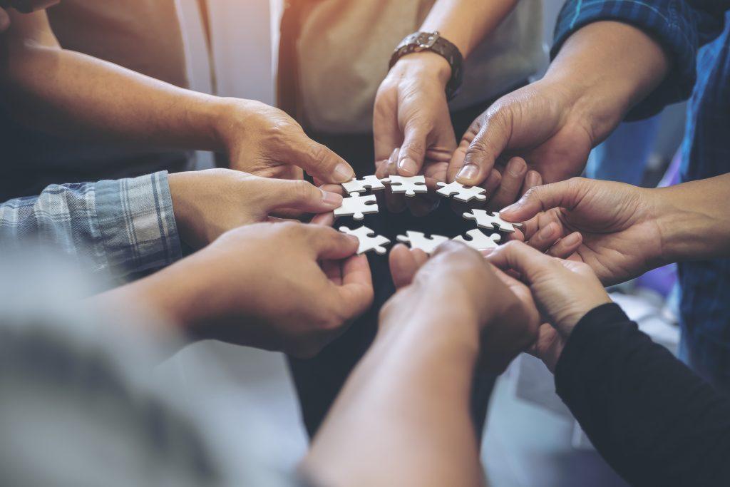 Gros plan sur plusieurs mains tenant ensemble une pièce de puzzle en cercle lors d'un coaching d'équipe