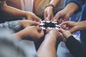 Gros plan sur plusieurs mains tenant ensemble une pièce de puzzle en cercle lors d'un coaching d'équipe