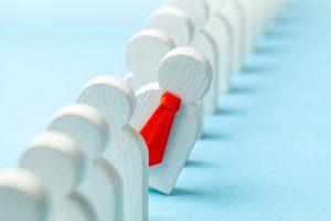 file d'attente de candidats représentés par des personnages en bois bois et un se détache des autres et porte une cravate rouge