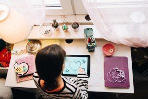 une enfant dessinant sur sa tablette tactile posée sur le bureau de sa chambre