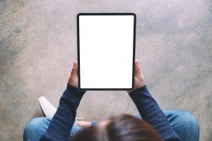 un homme assis en tailleur et tenant une tablette numérique entre ses mains