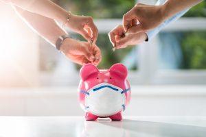 concept du crowfunding représenté par 4 mains déposant une pièce de monnaie dans une tirelire en forme de cochon rose