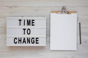le terme "time to change" écrit sur un petit tableau posé sur un bureau avec une feuille blanche et un stylo pour un entretien d'embauche