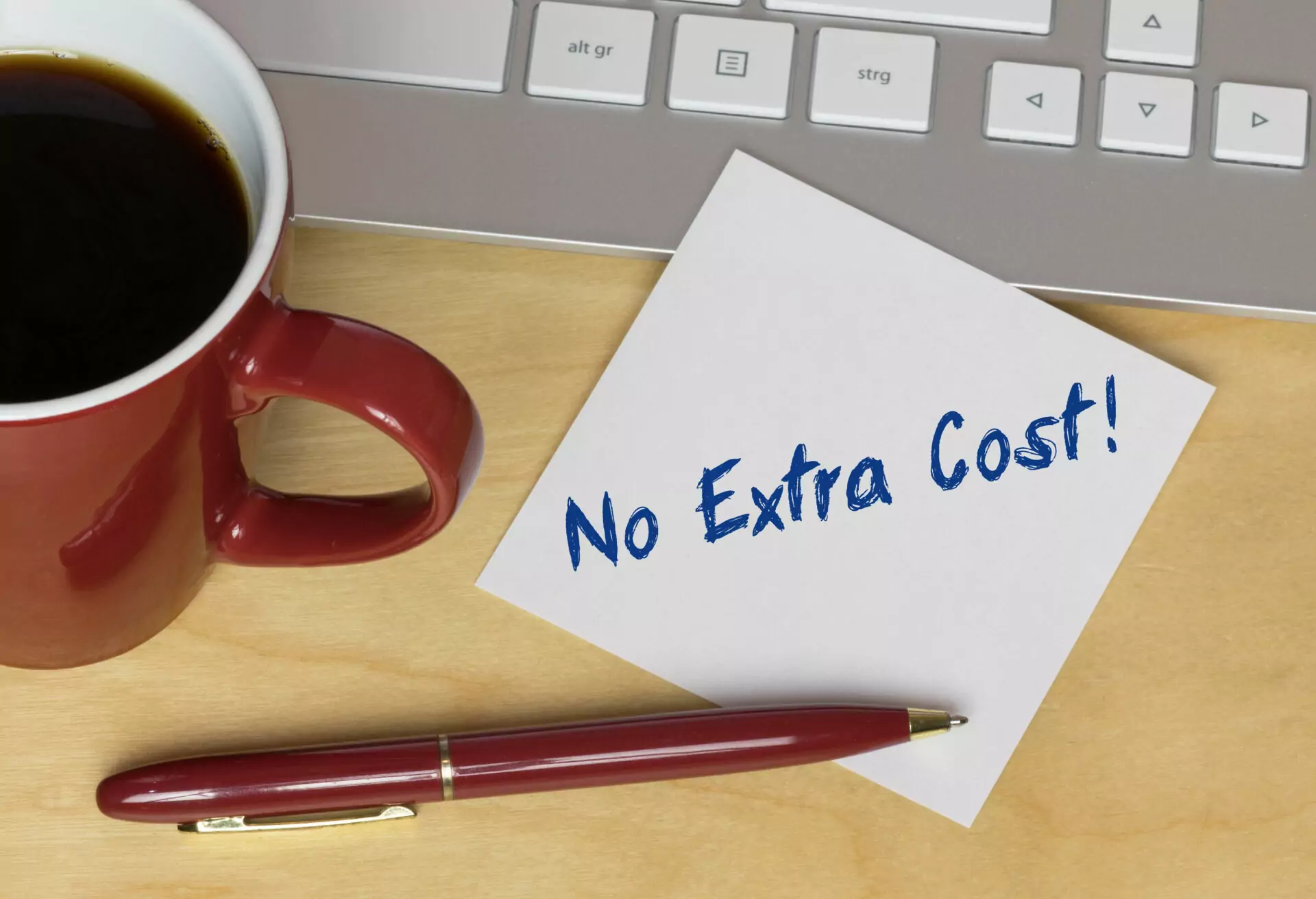 visuel d'une note où il est écrit no extra cost ! avec un stylo, un mug de café et un clavier d'ordinateur
